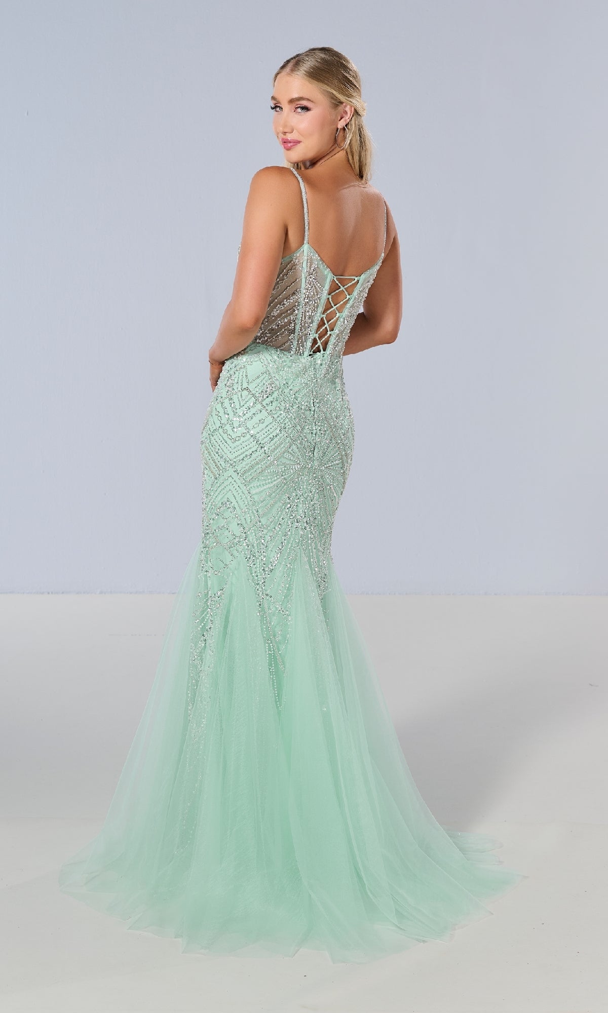A woman models the Tiffany 16218 long prom dress in mint green, featuring a sheer corset bodice, sequin-beaded mermaid details, and a lace-up back, posed against a plain light background.